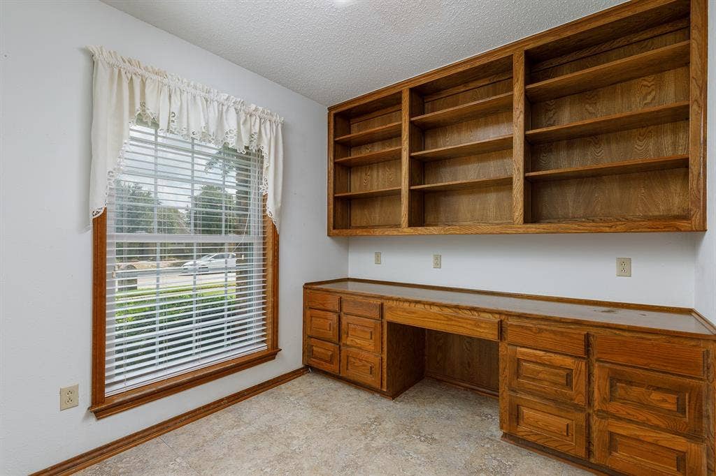 2526 Willowdale Drive, Carrollton, TX 75006 Built-in wood cabinetry with a desk area, overhead wood shelving, and a large window with horizontal blinds