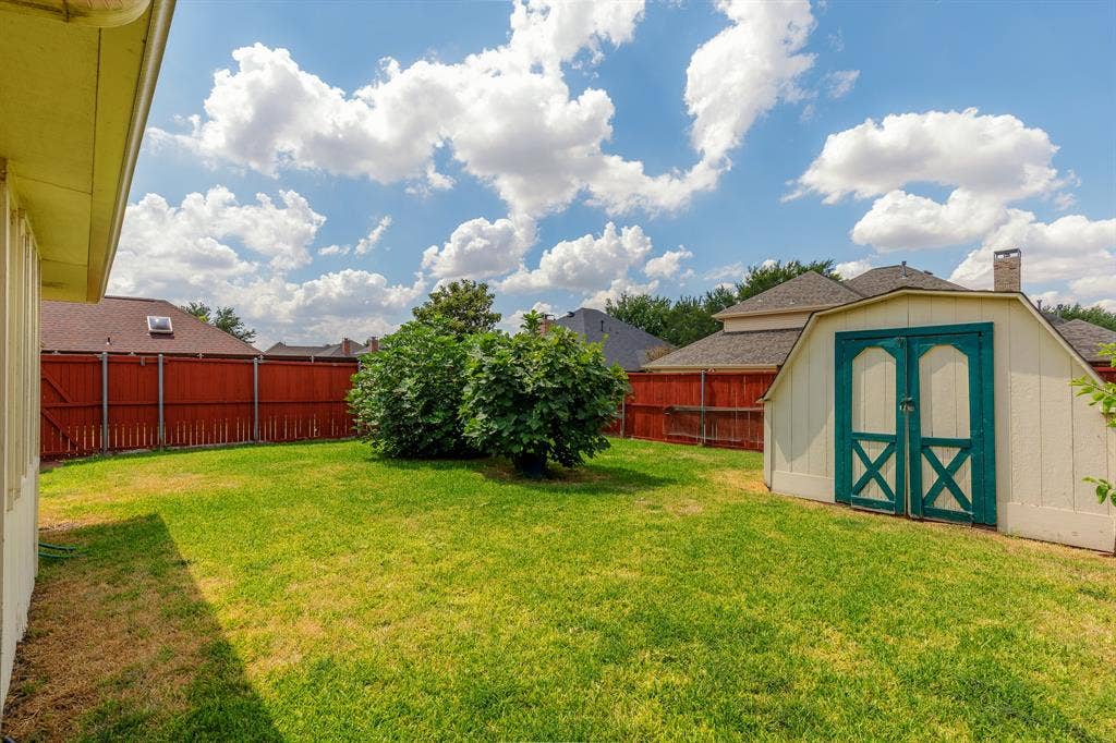 2526 Willowdale Drive, Carrollton, TX 75006 Expansive backyard featuring a manicured lawn, established shrubbery, full perimeter fencing, and a detached storage shed