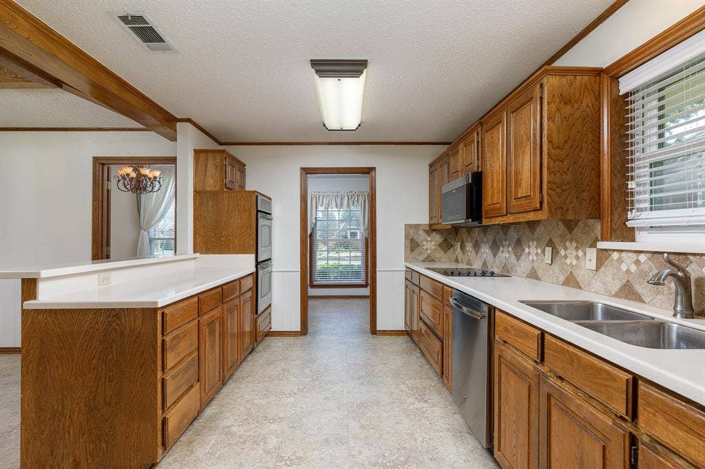2526 Willowdale Drive, Carrollton, TX 75006 Kitchen featuring natural wood cabinetry, white countertops, built-in stainless steel appliances, patterned tile backsplash, and a double basin sink