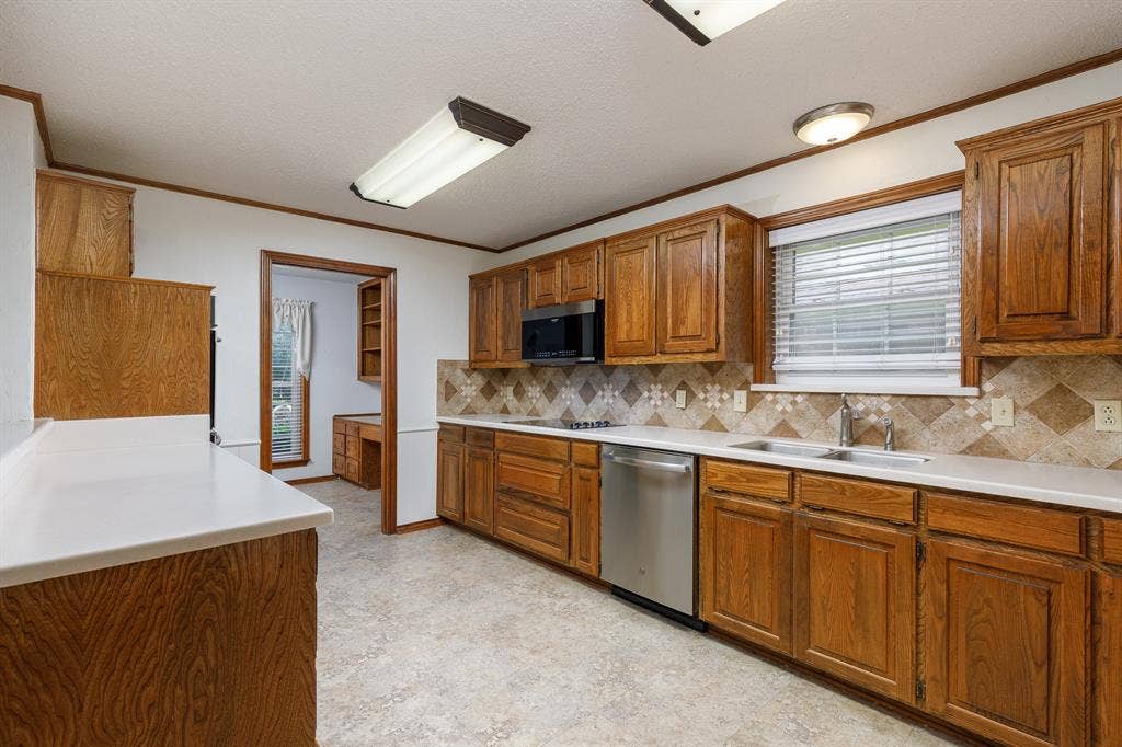 2526 Willowdale Drive, Carrollton, TX 75006 Wood cabinetry and white countertops define this kitchen space, featuring a stainless steel dishwasher, a built-in microwave, and a decorative tile backsplash