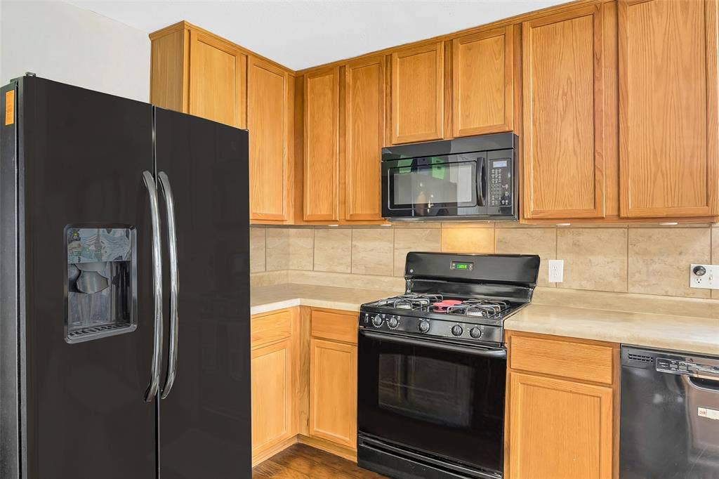 Wood-finish cabinetry, tile backsplash, built-in microwave, gas range, and a side-by-side refrigerator with ice/water dispenser