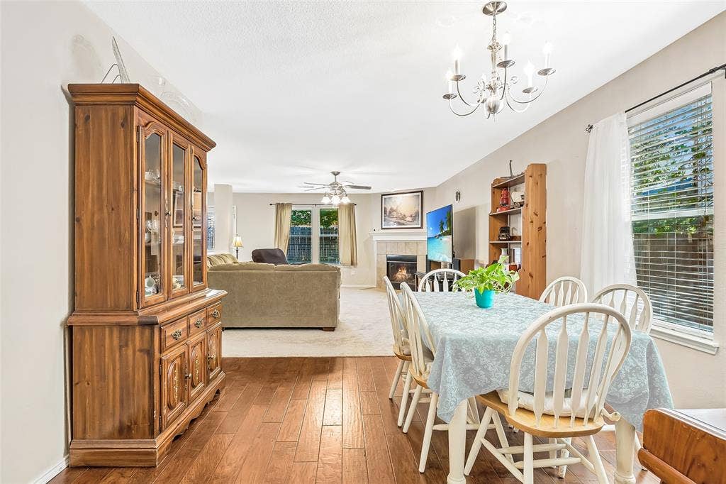 Wood-finish flooring, recessed lighting, and a chandelier illuminate the dining area, which transitions to a living space featuring a fireplace with a mantel