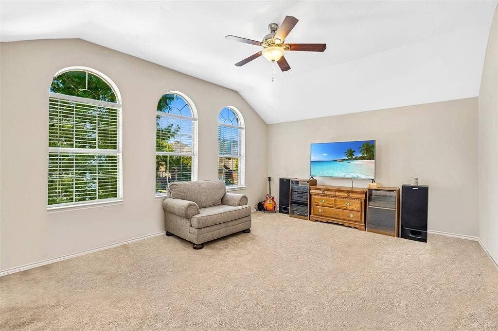 Vaulted ceilings with a ceiling fan, three arched windows, and light neutral carpeting