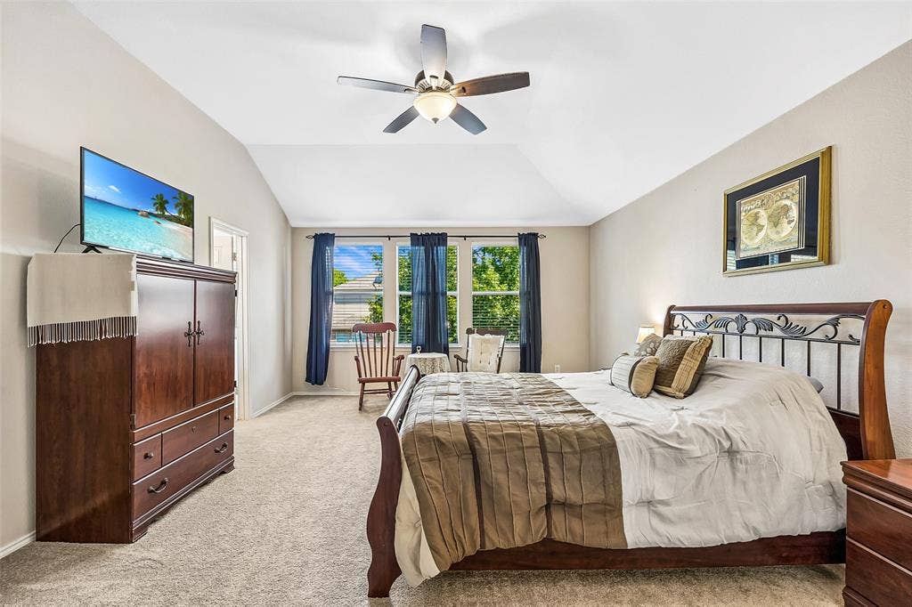 Vaulted ceiling with a ceiling fan, carpeted flooring, and a large window with blue curtains