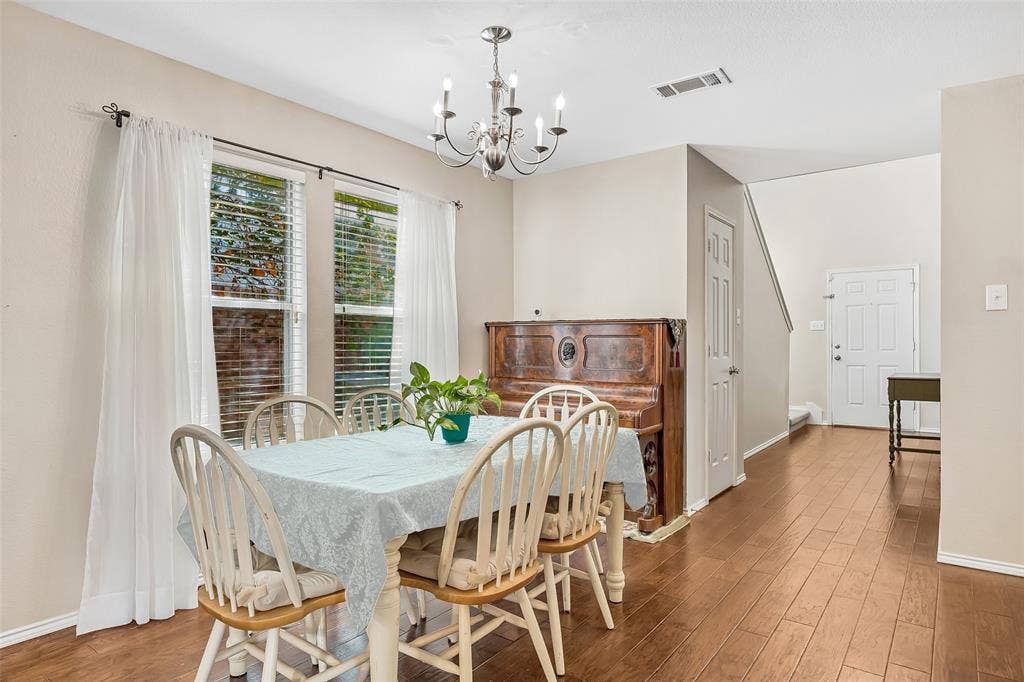 Wood-finish flooring throughout, dual windows with blinds, a polished chandelier, and a white paneled entry door