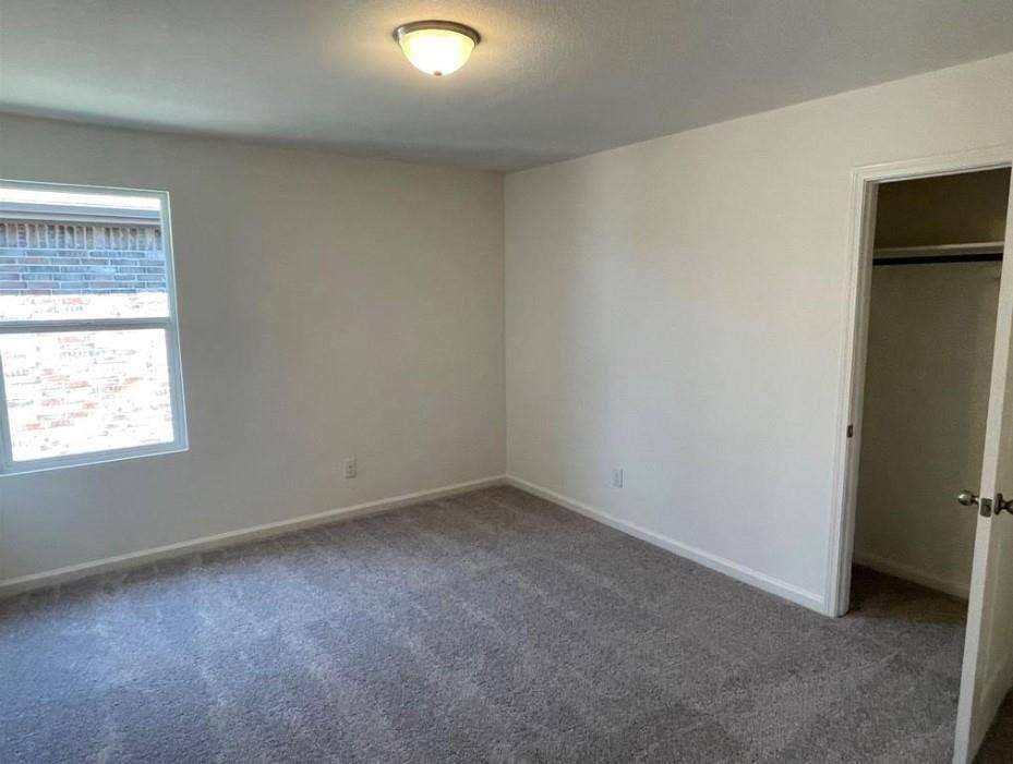 1903 Marquette Drive, Princeton, TX 75407 Wall-to-wall carpeting in a neutral tone, ceiling-mounted light fixture, white interior walls, and a window with a brick exterior visible