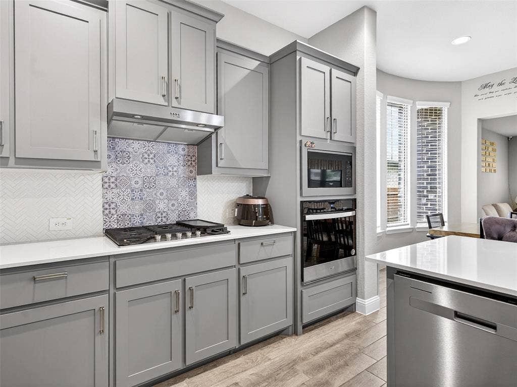 2504 Wren Lane, Denton, TX 76205 Gray shaker-style cabinetry with stainless steel hardware, white countertops, built-in microwave, integrated wall oven, and a gas cooktop with a decorative tile backsplash