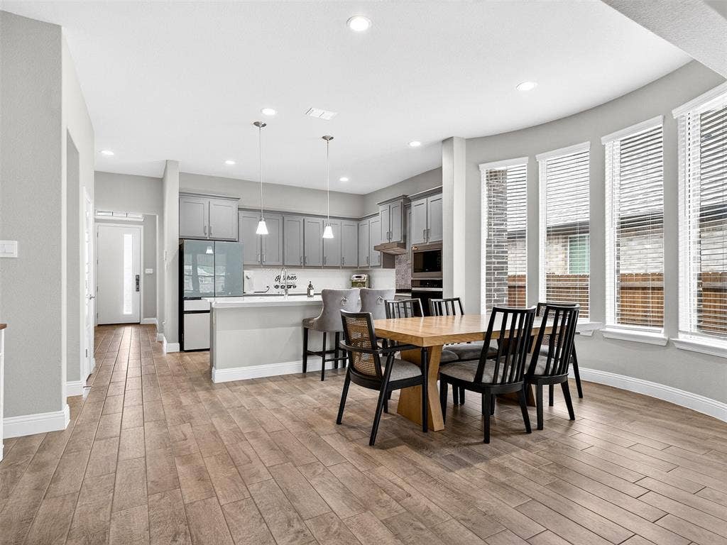 2504 Wren Lane, Denton, TX 76205 Wood-finish flooring throughout, curved wall with multiple windows, recessed lighting, and kitchen featuring gray cabinetry and pendant lights