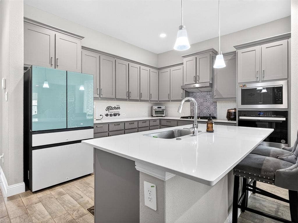 2504 Wren Lane, Denton, TX 76205 Kitchen featuring gray cabinetry, white countertops, stainless steel appliances, a center island with an undermount sink, and wood-finish flooring