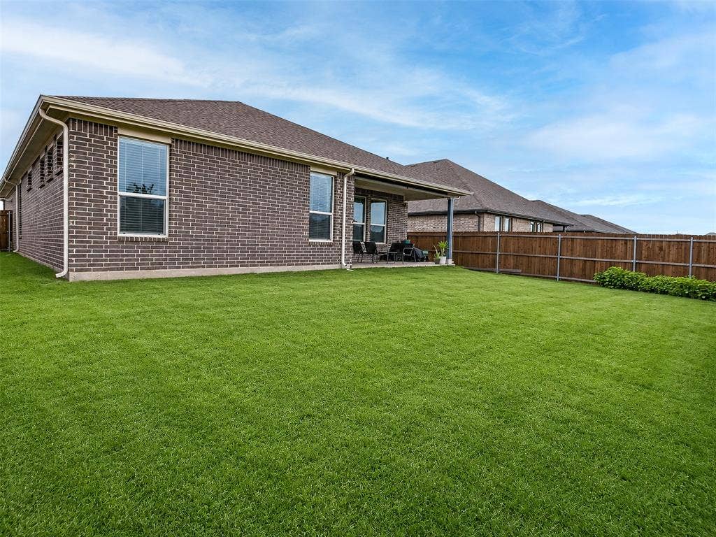 2504 Wren Lane, Denton, TX 76205 Expansive backyard featuring a manicured lawn, brick exterior, covered patio, and privacy fencing