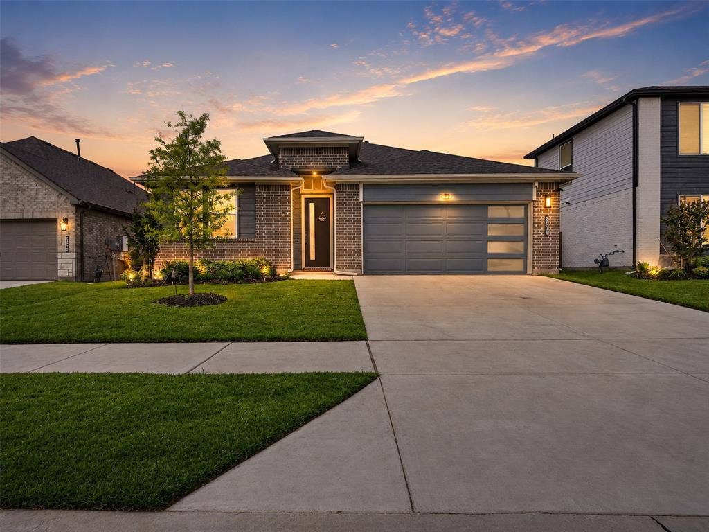 2504 Wren Lane, Denton, TX 76205 Brick and siding exterior with a dark roof, concrete driveway, and attached two-car garage featuring frosted glass panels