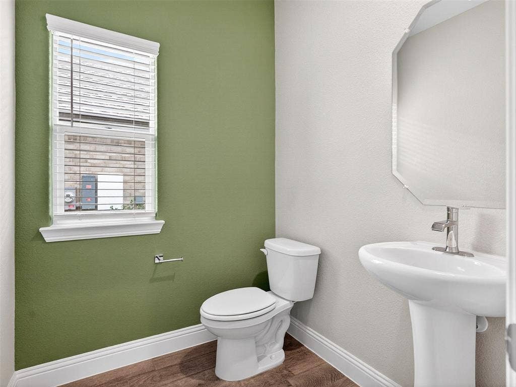 2504 Wren Lane, Denton, TX 76205 Pedestal sink with chrome-finish faucet, elongated toilet, wood-finish flooring, and a window with blinds
