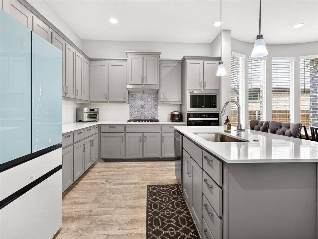 2504 Wren Lane, Denton, TX 76205 Kitchen featuring light gray cabinetry, white countertops, wood-finish flooring, a patterned tile backsplash, and a large center island with an integrated sink