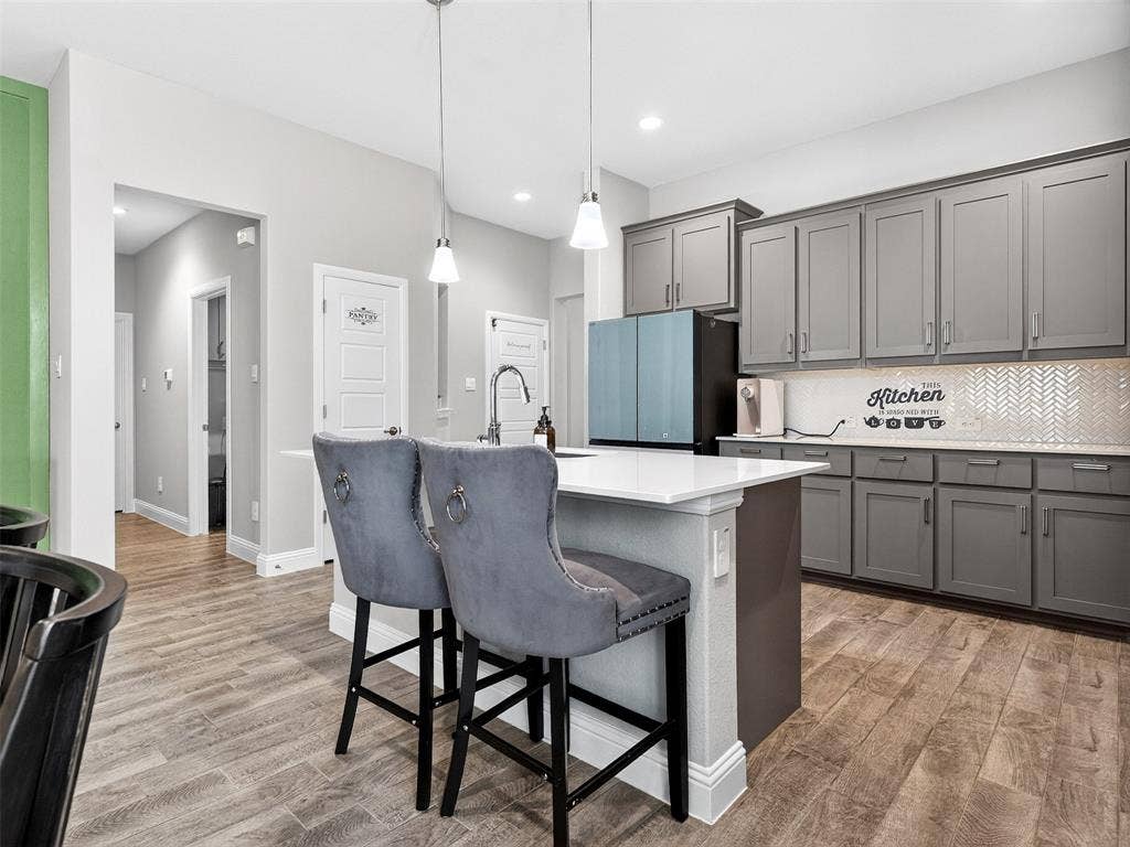 2504 Wren Lane, Denton, TX 76205 Kitchen featuring an island with a white countertop, gray cabinetry, wood-finish flooring, and a white herringbone tile backsplash