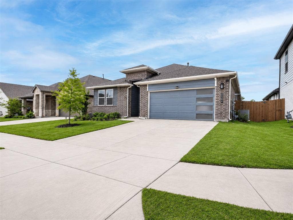 2504 Wren Lane, Denton, TX 76205 Brick exterior with gray siding accents, attached two-car garage with frosted panel inserts, concrete driveway, and established front landscaping