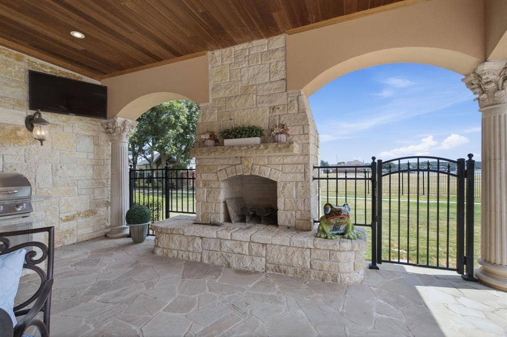 Covered patio featuring a stone fireplace, wood-finish ceiling, stone flooring, and wrought iron fencing
