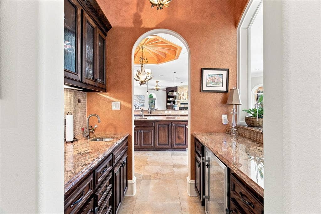 Wet bar featuring granite countertops, dark wood cabinetry, a built-in sink, and a beverage refrigerator