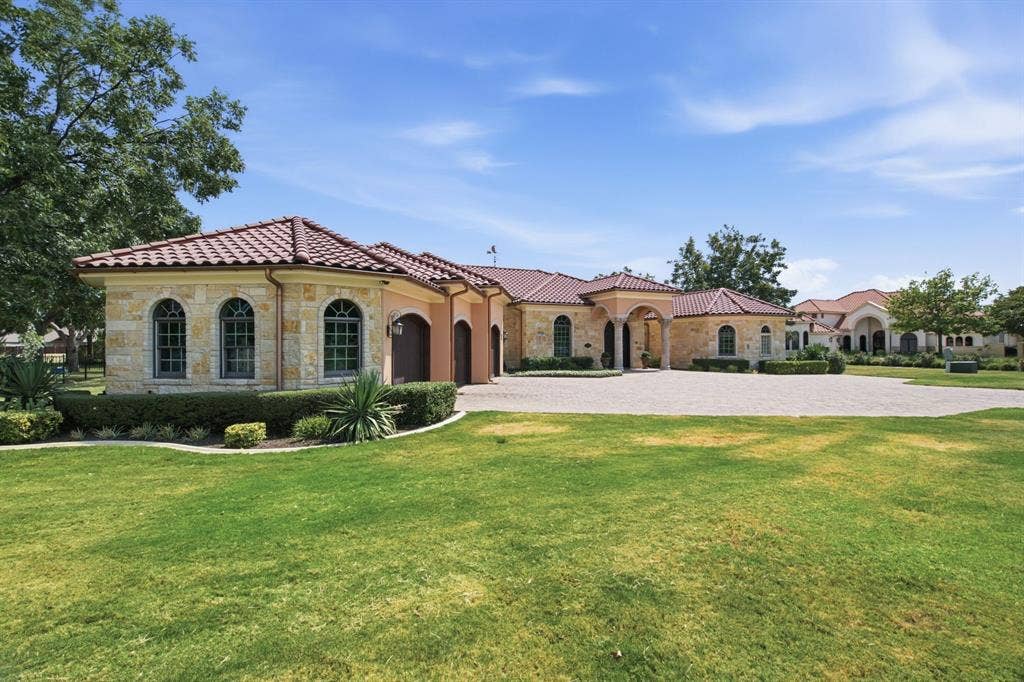 Stone exterior with arched windows, tile roofing, a circular driveway, and mature landscaping