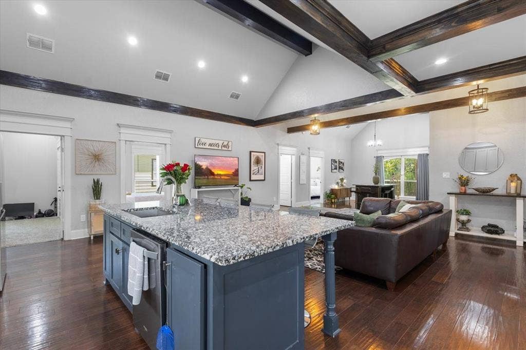 16136 County Road 1134=, Tyler, TX 75709 Open-concept living space with vaulted ceilings, exposed wood beams, wood-finish flooring, a kitchen island with stone countertops, and recessed lighting