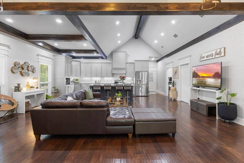 16136 County Road 1134=, Tyler, TX 75709 Open-concept living space with dark wood-finish flooring, vaulted ceiling with exposed beams, recessed lighting, and a modern kitchen featuring light gray cabinetry and stainless steel appliances
