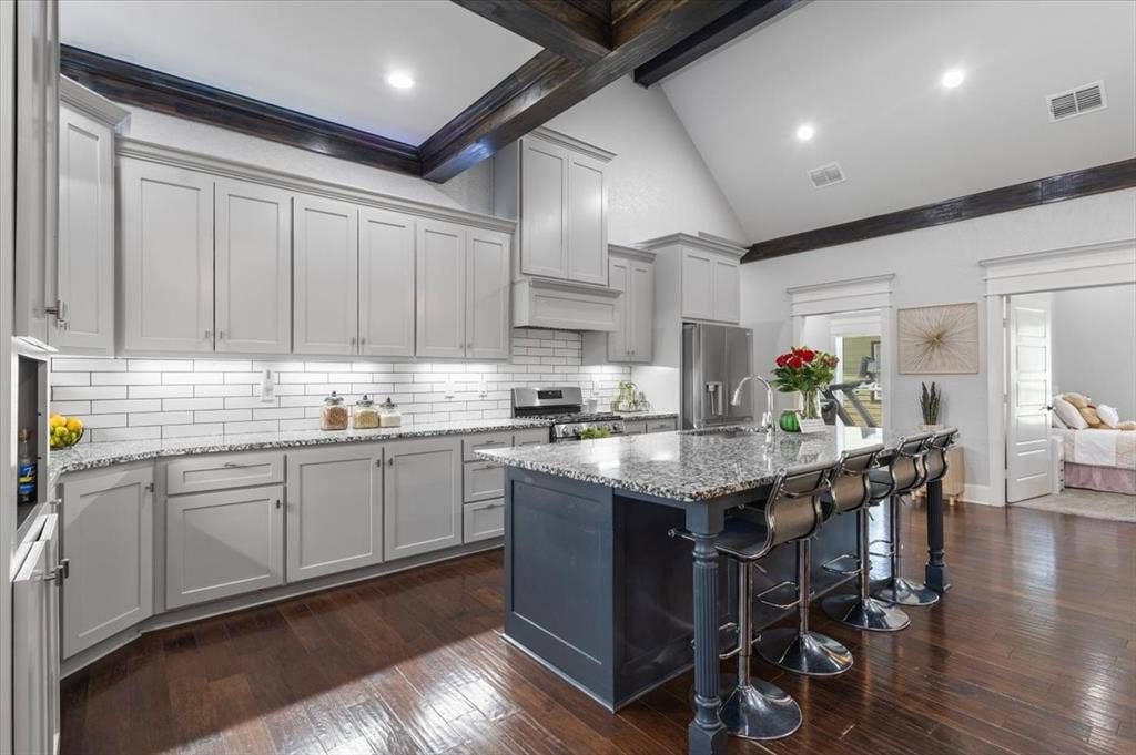 16136 County Road 1134=, Tyler, TX 75709 Kitchen featuring a vaulted ceiling with exposed beams, wood-finish flooring, a central island with a granite countertop, light-colored cabinetry, and a subway tile backsplash