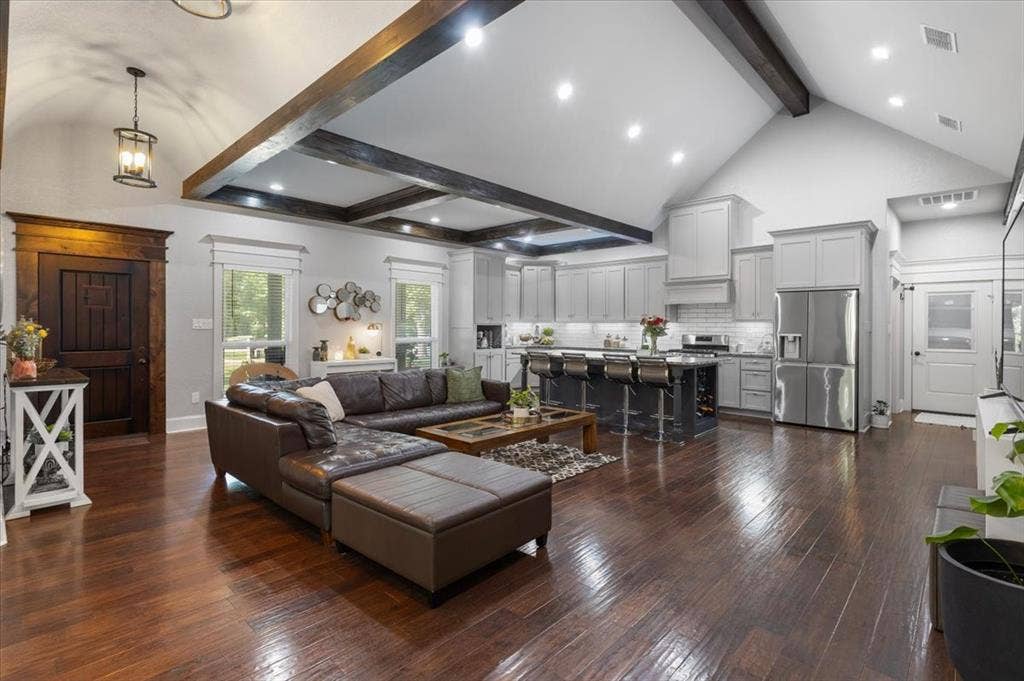 16136 County Road 1134=, Tyler, TX 75709 Vaulted ceiling with exposed wood beams, rich wood-finish flooring, a kitchen featuring stainless steel appliances, light gray cabinetry, and a dark island with seating