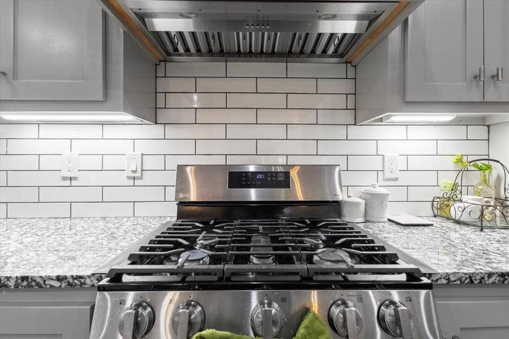 16136 County Road 1134=, Tyler, TX 75709 Stainless steel gas range with a coordinating range hood, white subway tile backsplash, light grey cabinetry, and speckled countertops