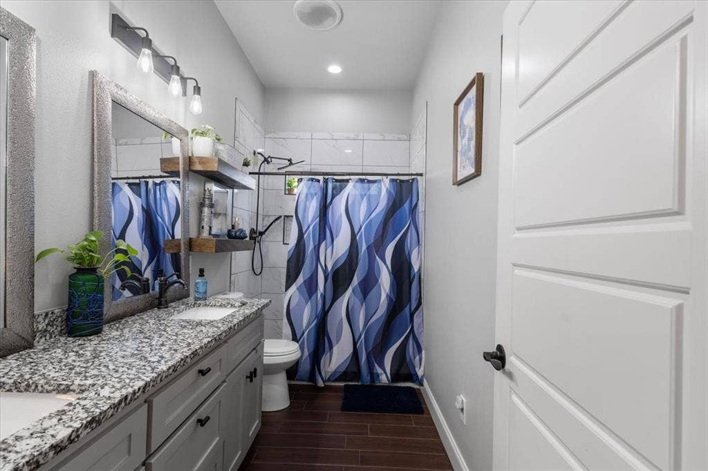 16136 County Road 1134=, Tyler, TX 75709 Dual vanity with granite countertop, wood-finish flooring, white shower tile, and a white interior door with contemporary paneling