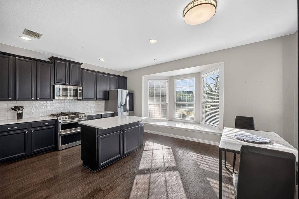 7880 Oxer Drive, Irving, TX 75063 Kitchen with dark cabinetry, stainless steel appliances, a center island with a white countertop, and wood-finish flooring