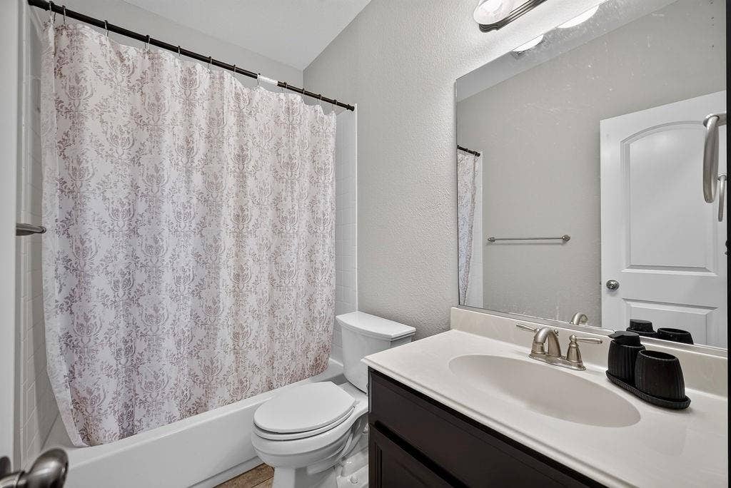 7880 Oxer Drive, Irving, TX 75063 Bathtub with shower, toilet, dark wood-finish vanity with white countertop, integrated sink, and an overhead vanity light fixture