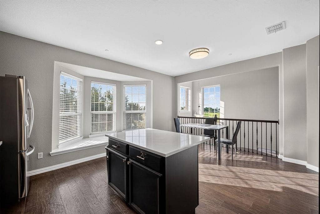 7880 Oxer Drive, Irving, TX 75063 Bay window with seating, recessed lighting, wood-finish flooring, central island with solid surface countertop, and iron baluster railing