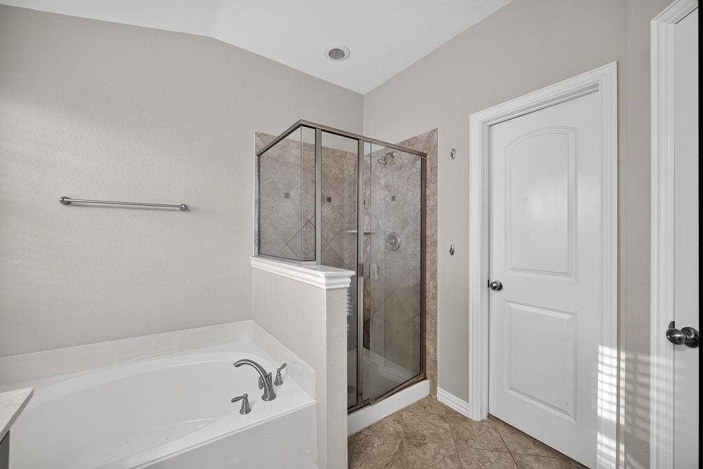 7880 Oxer Drive, Irving, TX 75063 Enclosed glass-panel shower with tiled surround, adjacent soaking tub with deck-mounted faucet, and tile flooring