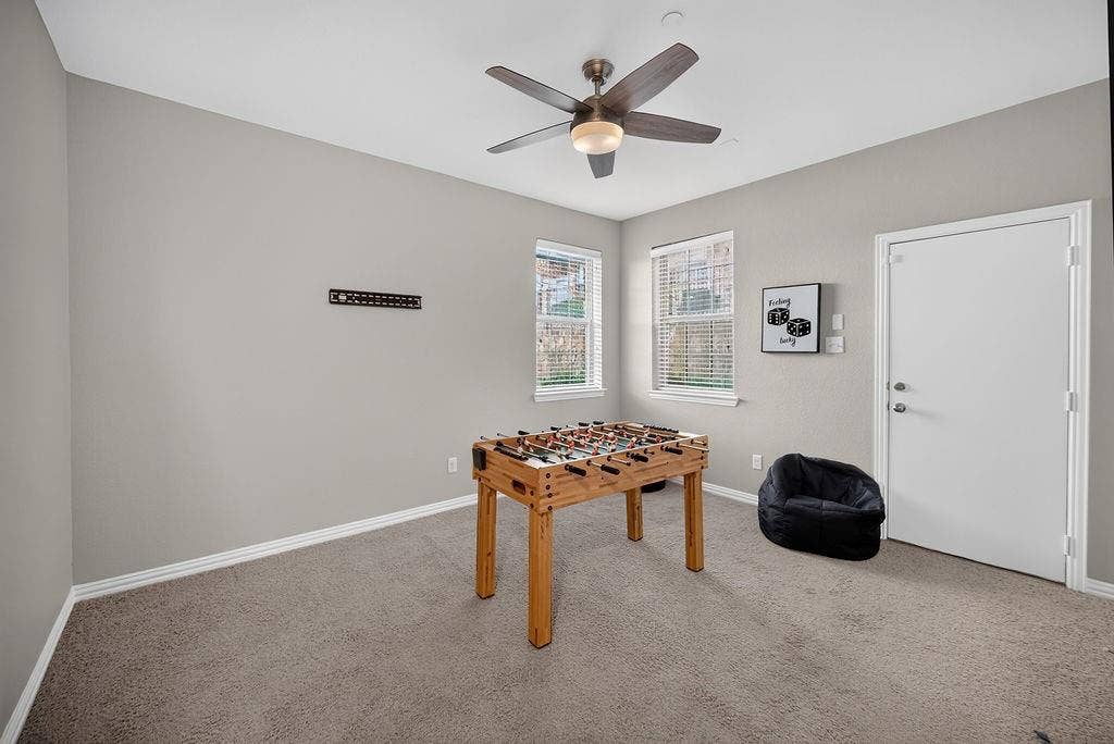 7880 Oxer Drive, Irving, TX 75063 Neutral-toned carpeting, ceiling fan with integrated lighting, two windows with blinds, and a white door with brushed nickel hardware