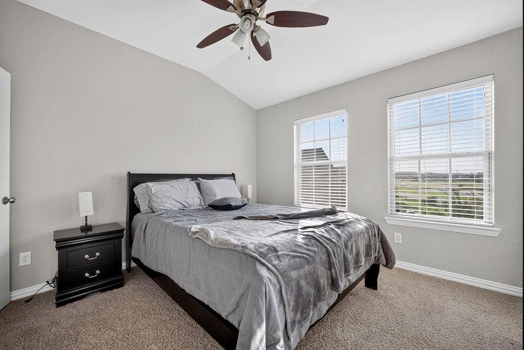 7880 Oxer Drive, Irving, TX 75063 Vaulted ceiling with a ceiling fan, two double-hung windows with blinds, and soft carpet flooring