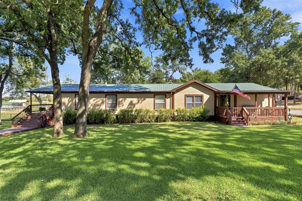 18404 Pine Drive, Eustace, TX 75124 Light-colored siding exterior with a green metal roof, a covered front porch, and an additional covered side porch