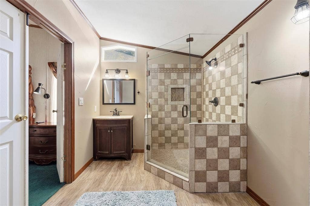 18404 Pine Drive, Eustace, TX 75124 Glass-enclosed shower with checkerboard tiling, wood-finish flooring, dark wood vanity with integrated sink, and bronze fixtures