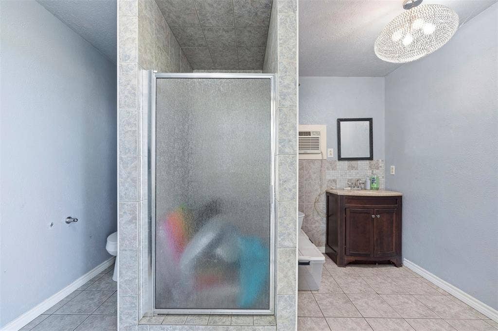 18404 Pine Drive, Eustace, TX 75124 Frosted glass shower enclosure, wood-finish vanity with countertop, tiled flooring, and decorative overhead lighting