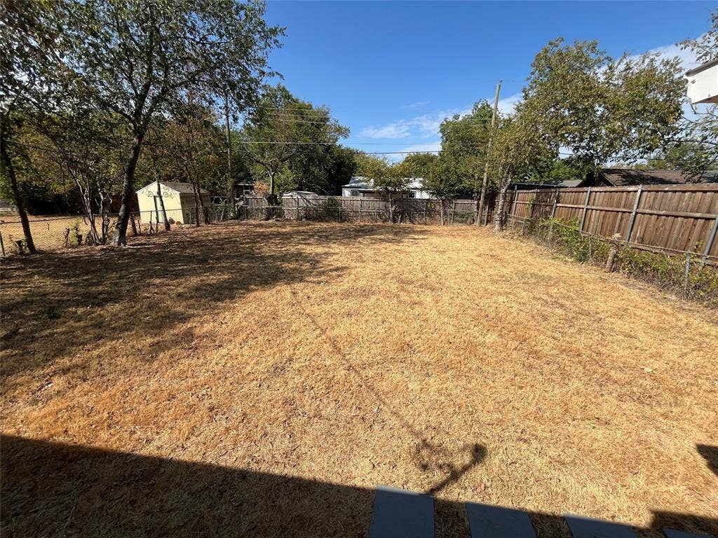427 NE 38th Street, Grand Prairie, TX 75050 Expansive backyard area with a perimeter wood fence, mature trees, and a visible storage shed