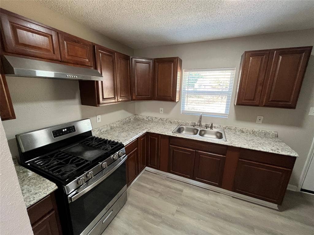 427 NE 38th Street, Grand Prairie, TX 75050 Kitchen featuring wood-finish cabinetry, stainless steel appliances, granite-look countertops, a double basin sink, and wood-look flooring