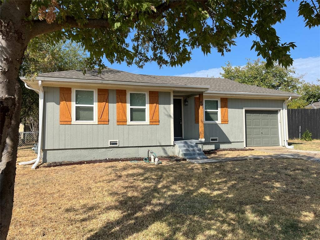 427 NE 38th Street, Grand Prairie, TX 75050 Single-story residence featuring a gray exterior, wood-finish shutters, a covered entry, and an attached garage