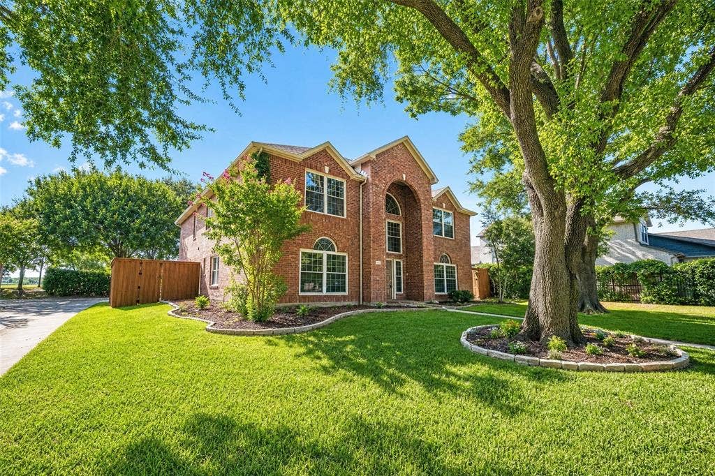 3041 Hillingdon Drive, Richardson, TX 75082 Traditional brick exterior with arched entry, lush green lawn, mature trees, and landscaped beds with stone edging