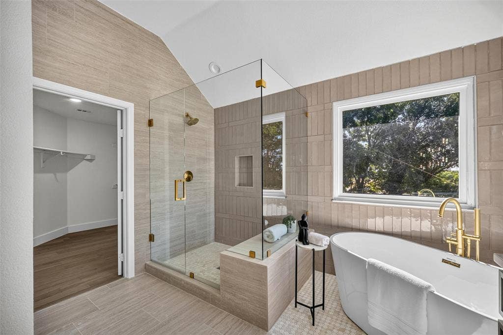 3041 Hillingdon Drive, Richardson, TX 75082 Free-standing soaking tub with brass fixtures, glass-enclosed shower with brass hardware, tiled shower niche, wood-finish flooring, and a walk-in closet