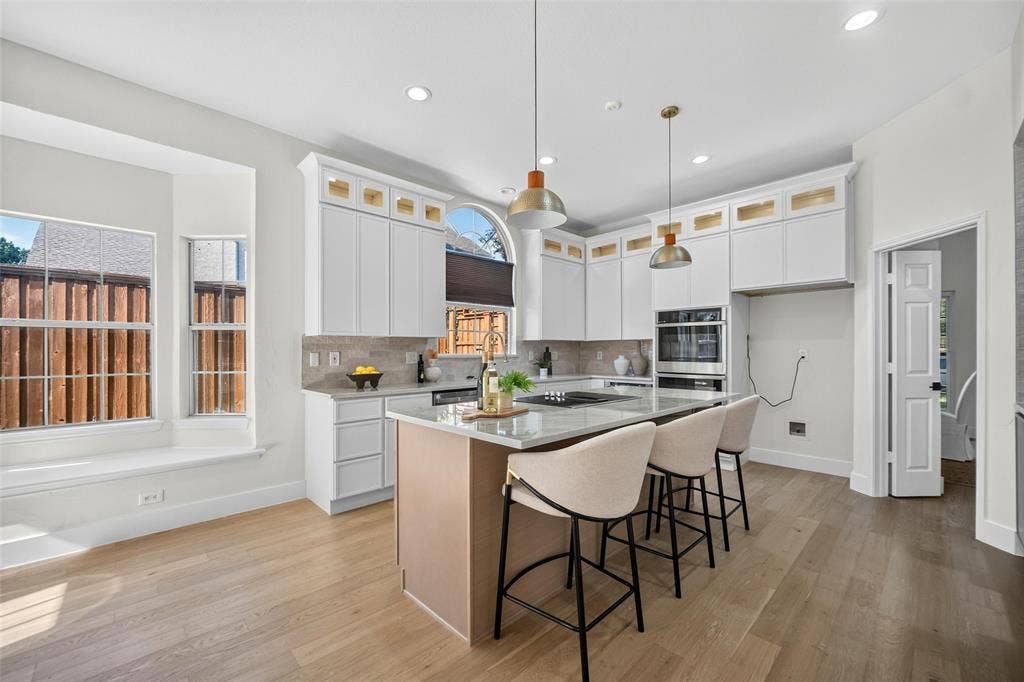 3041 Hillingdon Drive, Richardson, TX 75082 Light wood-finish flooring, white cabinetry with gold-tone accents, an island with countertop seating, a built-in oven, and recessed lighting
