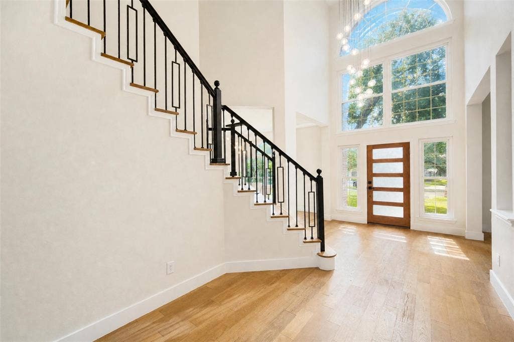 3041 Hillingdon Drive, Richardson, TX 75082 Two-story entryway featuring light wood-finish flooring, a contemporary wood-panel entry door, and a grand staircase with wrought iron balusters and wood treads