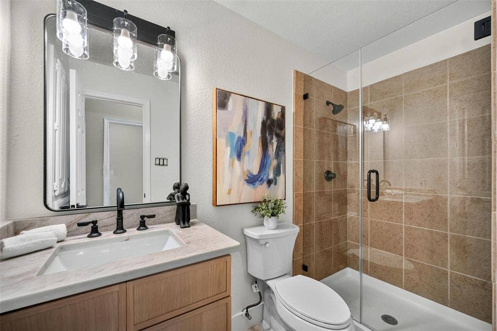 3041 Hillingdon Drive, Richardson, TX 75082 Bathroom featuring a glass-enclosed shower, light wood-finish vanity with an undermount sink, stone-finish countertop, and black-finish fixtures