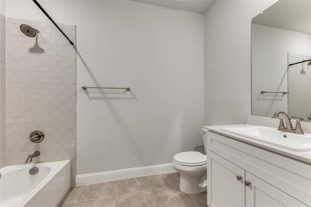 Full bath featuring vanity, toilet,  shower combination, baseboards, and tile patterned flooring