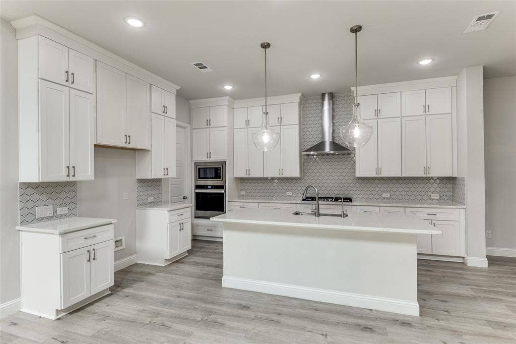 Kitchen featuring stainless steel appliances, wall chimney range hood, light countertops, decorative backsplash, and recessed lighting
