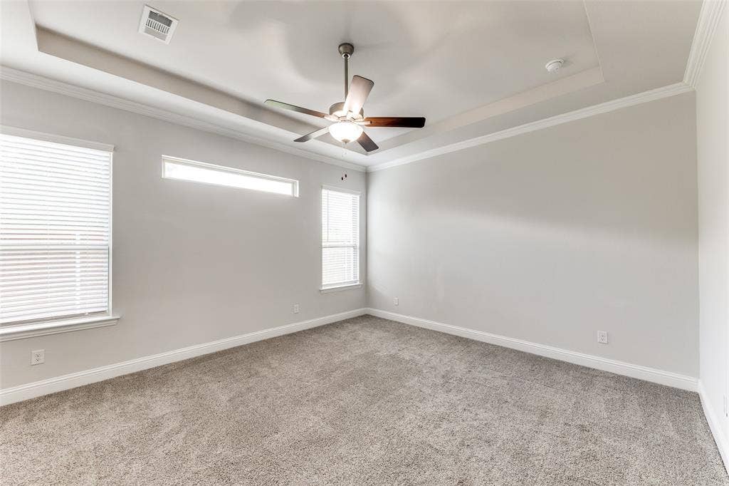Spare room with a tray ceiling, carpet, ceiling fan, baseboards, and ornamental molding