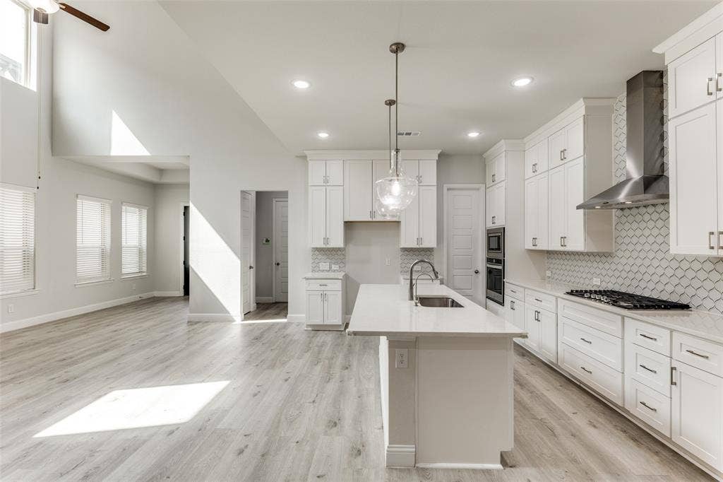 Kitchen with wall chimney range hood, a sink, stainless steel appliances, tasteful backsplash, and light countertops