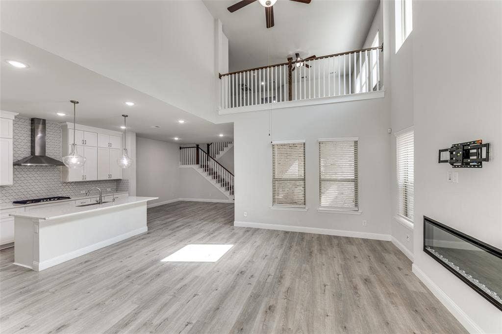 Unfurnished living room with a ceiling fan, light wood-style flooring, a high ceiling, a sink, and baseboards